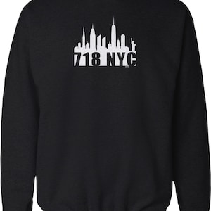May include: Black sweatshirt featuring a white graphic of the New York City skyline, including the Statue of Liberty and the text "718 NYC". The design is centered on the chest of the sweatshirt.
