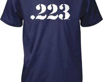 May include: A navy blue short-sleeve t-shirt featuring the white text .223 printed across the chest. The font has a distressed, textured appearance. The garment has a crew neckline and a standard fit, providing a simple and clean look.