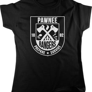 May include: A black short-sleeved t-shirt featuring a white graphic emblem. The emblem displays the text PAWNEE RANGERS, 1882, and PREPARE SURVIVE, along with crossed axes, a raccoon tail, arrows, and a flame icon centered on the chest.