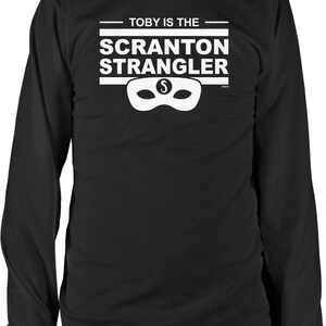May include: Black long-sleeve t-shirt with white text that reads "Toby is the Scranton Strangler" and a white mask with a dollar sign on it.