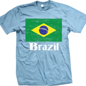 May include: A light blue t-shirt with a distressed image of the Brazilian flag and the word "Brazil" in white text.