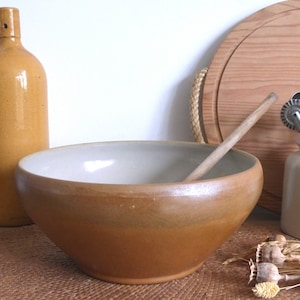 May include: A large, brown ceramic mixing bowl with a white interior. The bowl is sitting on a woven brown mat.