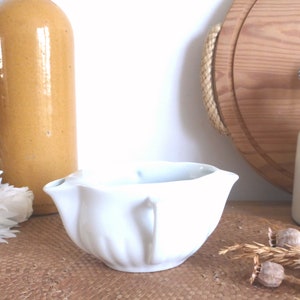 Puede incluir: Salsera de cerámica blanca con borde acanalado y dos asas. La salsera está sobre una superficie marrón.