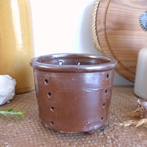 Könnte beinhalten: Eine braune Keramik-Käseform mit Löchern zum Abtropfen. Die Form hat einen leicht abgerundeten Boden und eine glatte, glasierte Oberfläche.