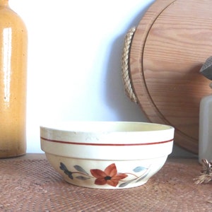 Puede incluir: Un tazón de cerámica blanco con un diseño floral rojo y verde. El tazón tiene un borde de color crema y una fina franja roja alrededor de la parte superior.