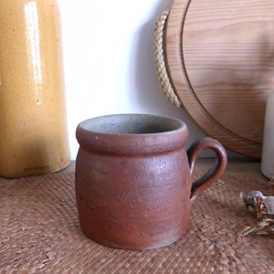 May include: A brown ceramic mug with a handle. The mug is sitting on a woven mat.