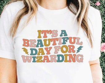 May include: White t-shirt with a colorful graphic that reads "It's a beautiful day for wizarding".