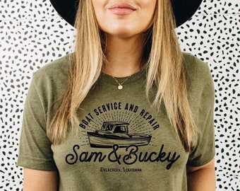 May include: A green t-shirt with a black graphic of a boat and the text "Boat Service and Repair Sam & Bucky Delacroix, Louisiana".