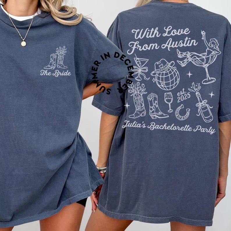May include: A dark blue t-shirt with a white graphic design on the back. The design includes the text "With Love From Austin", a horseshoe, a bottle of champagne, a glass of wine, a cowboy hat, a disco ball, and a pair of cowboy boots. The text "Summer in December" is written in a circle around the design. The text "est. 2025" and "Julia's Bachelorette Party" are also included in the design. The front of the shirt has the text "The Bride" and a pair of cowboy boots.