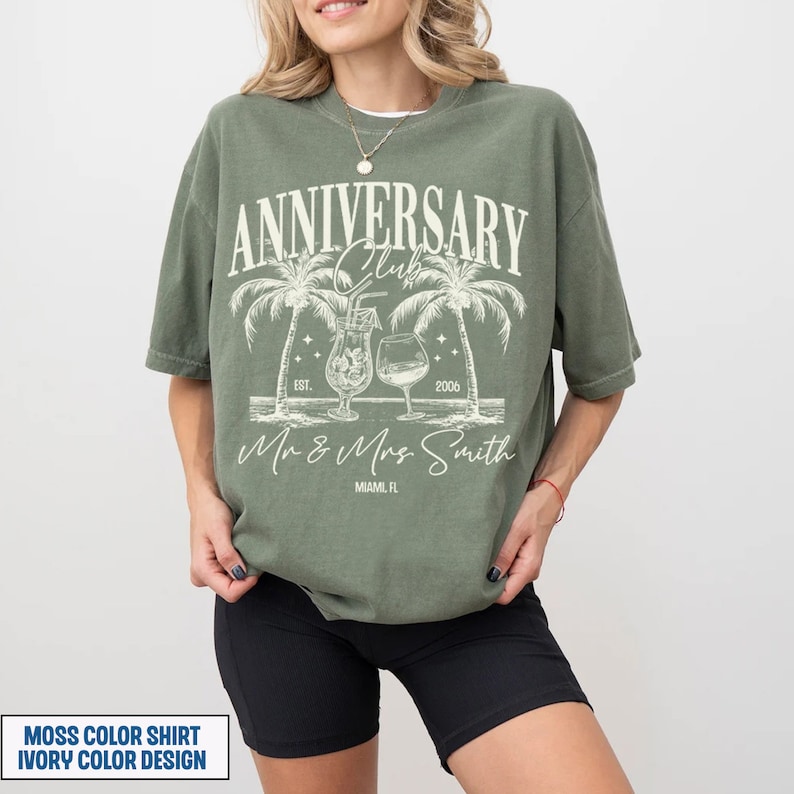 K&ouml;nnte beinhalten: Ein moosgr&uuml;nes T-Shirt mit einem Vintage-Design mit Palmen, Cocktails und dem Text "Anniversary Club Est. 2006 Mr & Mrs Smith Miami, FL". Das Design ist in Elfenbein.