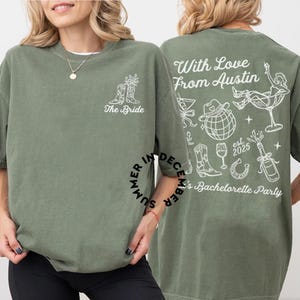 May include: Two green t-shirts with white text and graphics. The front shirt says "The Bride" with a pair of cowboy boots and flowers. The back shirt says "With Love From Austin" with a variety of graphics including cowboy boots, a glass of wine, a horseshoe, and a bottle of champagne. The text also says "Summer in December's Bachelorette Party est. 2025."
