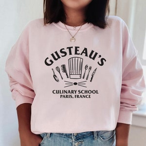 May include: Pink sweatshirt with a black graphic of a chef's hat and kitchen utensils. The text "Gusteau's Culinary School Paris, France" is printed below the graphic.