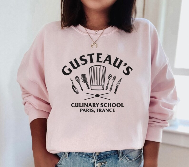 May include: Pink sweatshirt with a black graphic of a chef's hat and kitchen utensils. The text "Gusteau's Culinary School Paris, France" is printed below the graphic.
