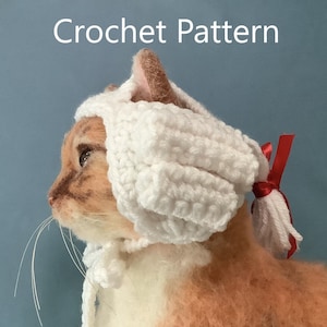May include: A white crocheted cat hat with a red ribbon. The hat is worn by a cat with brown and white fur.