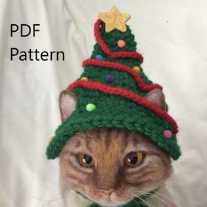 May include: A brown and orange cat wearing a green knitted Christmas tree hat with red yarn and colorful pom-poms. The hat has a gold star on top. The cat is looking at the camera. PDF Pattern.