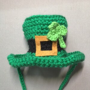 K&ouml;nnte beinhalten: Gr&uuml;ner geh&auml;kelter Leprechaun-Hut mit einem schwarzen und braunen G&uuml;rtel und einem gr&uuml;nen Kleeblatt oben. Der Hut hat eine lange gr&uuml;ne Schnur.