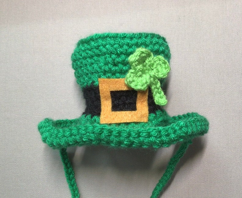 K&ouml;nnte beinhalten: Gr&uuml;ner geh&auml;kelter Leprechaun-Hut mit einem schwarzen und braunen G&uuml;rtel und einem gr&uuml;nen Kleeblatt oben. Der Hut hat eine lange gr&uuml;ne Schnur.