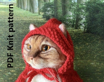 May include: A plush cat wearing a red knitted hooded cape. The cat has brown and white fur and large, expressive eyes.