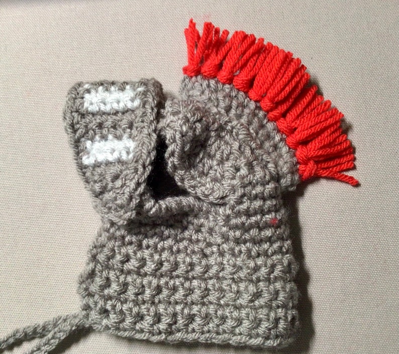 K&ouml;nnte beinhalten: Grauer H&auml;kelhelm mit roter Fransenborte oben. Der Helm hat ein wei&szlig;es H&auml;kelmuster an der Seite.
