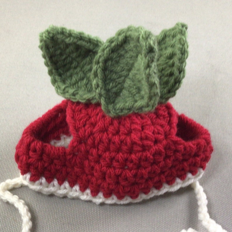 May include: Red and white crocheted baby booties with green crocheted leaves on top.
