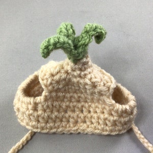 May include: A crocheted cream-colored hat with a green crocheted leaf on top. The hat has two holes on the sides for ears.