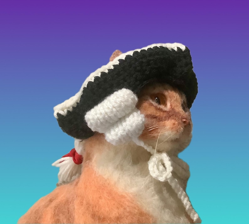 May include: A ginger cat wearing a handmade crochet hat with a black brim and white accents. The hat has white ear coverings and a white tie. The cat is set against a gradient blue and purple background.