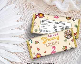 May include: A yellow and white chocolate bar wrapper with a groovy 70s theme. The wrapper features a peace sign, a rainbow, a disco ball, and the text "Let's get Groovy Emma is 2".