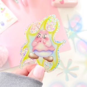 May include: A holographic sticker featuring a cartoon character with pink skin, a pink and blue dress, and yellow hair. The character is surrounded by a yellow flame design.