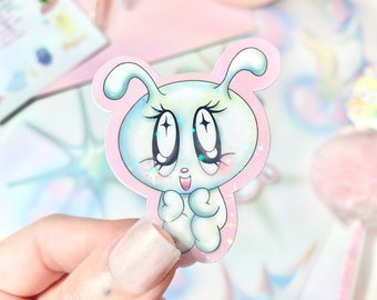 May include: A sticker featuring a cartoon character with large eyes, a pink body, and blue and white details. The character has a happy expression and is holding its hands together. The sticker has a holographic finish.