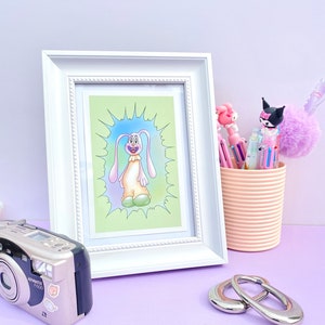 May include: A white framed print of a cartoon dog with a green background. The dog is pink and has a big smile. The dog is standing on a green patch of grass.