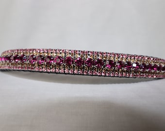 May include: A black leather dog collar with three rows of rhinestones. The top row features larger pink rhinestones, while the bottom two rows feature smaller pink and gold rhinestones.