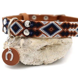 Peut inclure: Un collier pour chien en cuir marron avec un motif g&eacute;om&eacute;trique blanc, bleu marine et marron. Il est orn&eacute; de rivets argent&eacute;s et d'un anneau argent&eacute; avec une &eacute;tiquette en cuir marron et un charm en forme de fer &agrave; cheval.