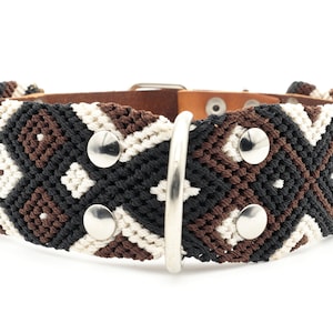 Puede incluir: Un collar para perro de color marrón, negro y blanco con una hebilla plateada. El collar está hecho de tejido tejido y tiene un respaldo de cuero.
