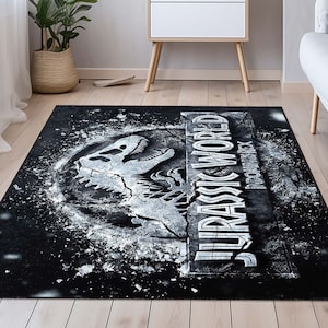 May include: Black rectangular rug with the Jurassic World logo in white. The logo features a dinosaur skull and the text "JURASSIC WORLD" in a distressed style. The rug has a dark, speckled background, suitable for a living room or bedroom.