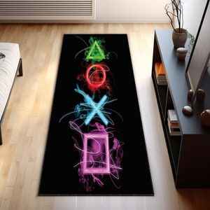 May include: A black and white rug with a design of the PlayStation controller symbols in neon colors. The symbols are a triangle, circle, X, and square.