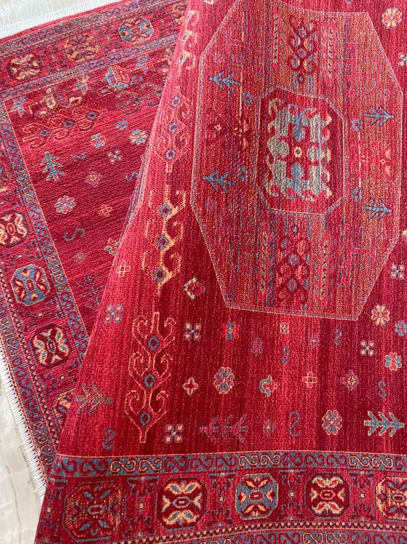 May include: A red rug with a geometric pattern in shades of blue, yellow, and cream. The rug has a fringe border.