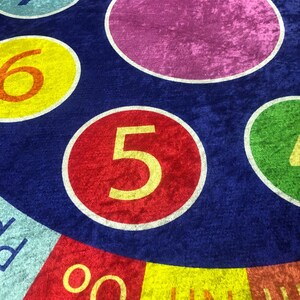 May include: A blue and red circular play mat with colorful circles featuring the numbers 1 through 7. The center circle is purple and the outer ring has the words "UN" and "OO" in yellow.