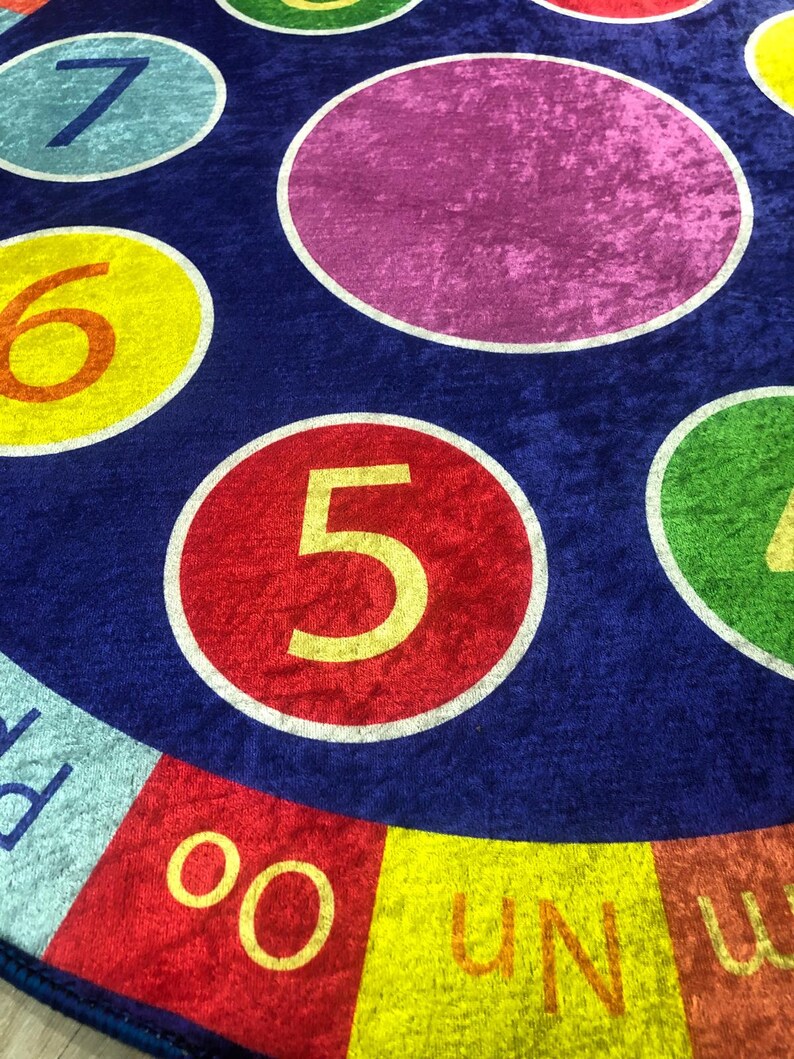 May include: A blue and red circular play mat with colorful circles featuring the numbers 1 through 7. The center circle is purple and the outer ring has the words "UN" and "OO" in yellow.