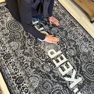 May include: A black and white patterned rug with the words "!KEEP" written in white letters.
