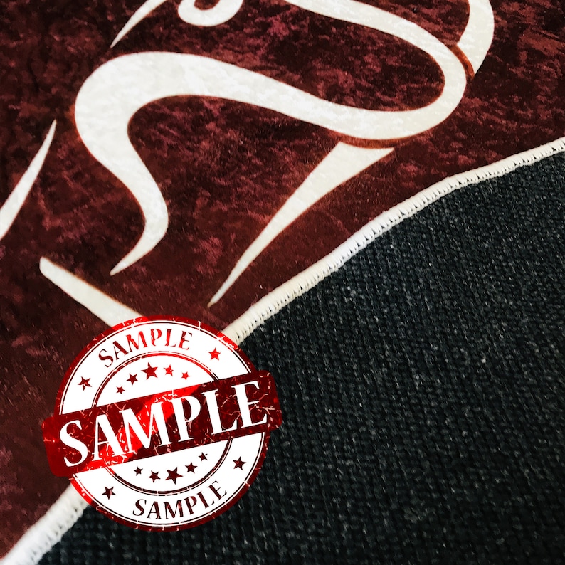 May include: Close-up of a red and white patterned rug with a red "SAMPLE" stamp. The rug has a white border and a black backing.
