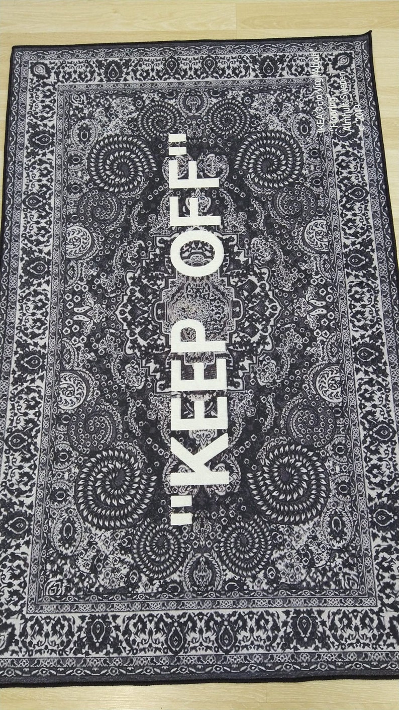 May include: Black and white rug with a traditional paisley pattern. The text "KEEP OFF!" is printed in white in the center of the rug.