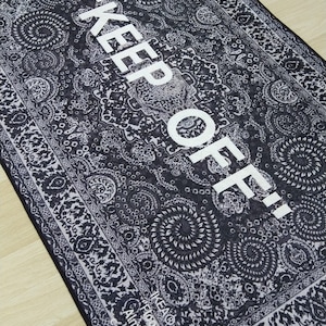 May include: Black and white patterned rug with the text "KEEP OFF!" in white. The rug has a border with a floral design. The text "IKEA Flooring" and "Almhult Sweden" is visible in the bottom right corner.