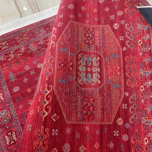 May include: A red rug with a geometric pattern in shades of blue, orange, and yellow. The rug has a fringe border.