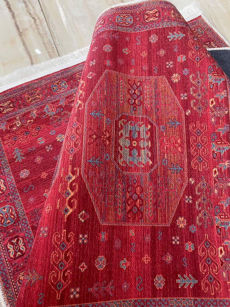 May include: A red rug with a geometric pattern in shades of blue, orange, and yellow. The rug has a fringe border.
