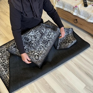 May include: A person is folding a black and white patterned rug. The rug has a geometric design with intricate details. The rug is folded in half and the person is holding the edges of the rug.