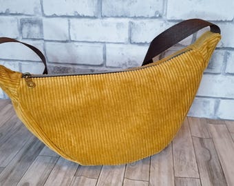 May include: Mustard yellow corduroy fanny pack with a brown strap and zipper closure. The bag has a curved shape and a brown strap for wearing around the waist or across the body. The bag is made of a soft corduroy fabric.