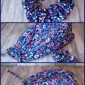 May include: A navy blue fabric scrub cap and matching scrunchie featuring a floral pattern with pink, white, and light blue petals and green leaves. The scrub cap has a rounded top, a gathered back, and two fabric ties for securing the fit.