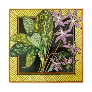 May include: A square tile with a yellow and orange border. The tile features a black background with a floral design of purple flowers and green leaves.