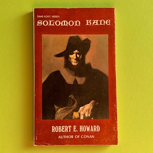 Könnte beinhalten: Ein Vintage-Taschenbuch mit dem Titel "Solomon Kane" von Robert E. Howard. Das Cover zeigt ein Porträt eines Mannes mit dunklem Hut und Umhang vor rotem Hintergrund. Das Buch gehört zur "Time-Lost Series".