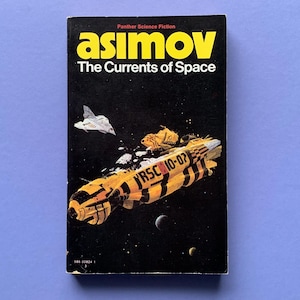 Könnte beinhalten: Vintage Taschenbuchcover für "The Currents of Space" von Asimov. Das Cover zeigt einen schwarzen Hintergrund mit einem gelb-schwarzen Raumschiff, einem weißen Raumschiff und Planeten. Titel und Autorenname sind gelb.
